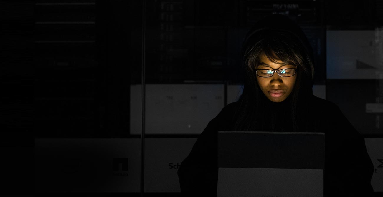 Frau schaut in einem dunklen Raum auf einen Laptop.